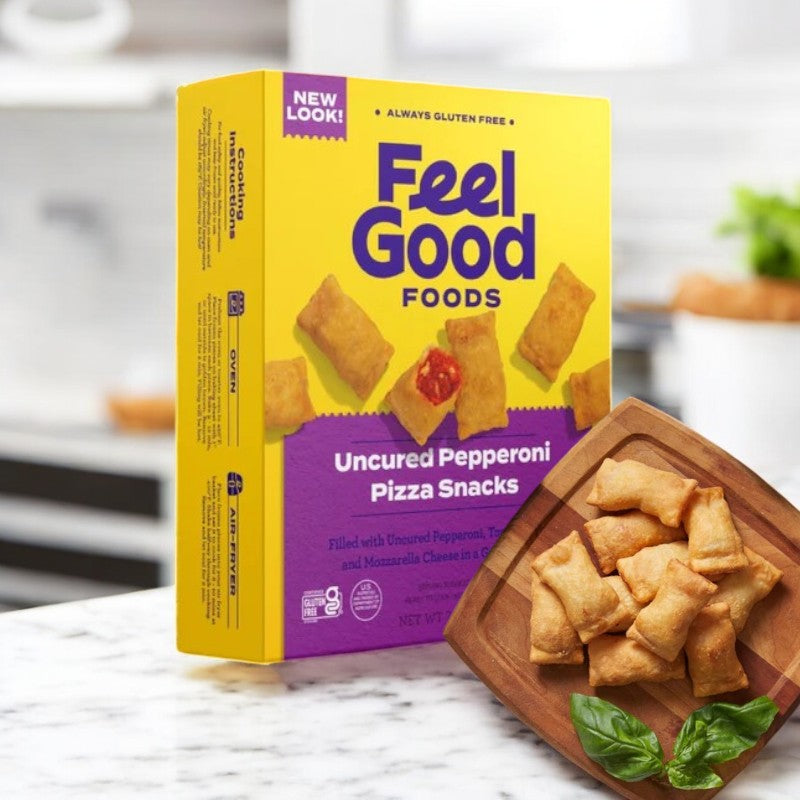 A box of Feel Good Foods Uncured Pepperoni Pizza Snacks with gluten-free crust is on the kitchen counter next to a wooden plate of ready-to-eat snacks garnished with basil.