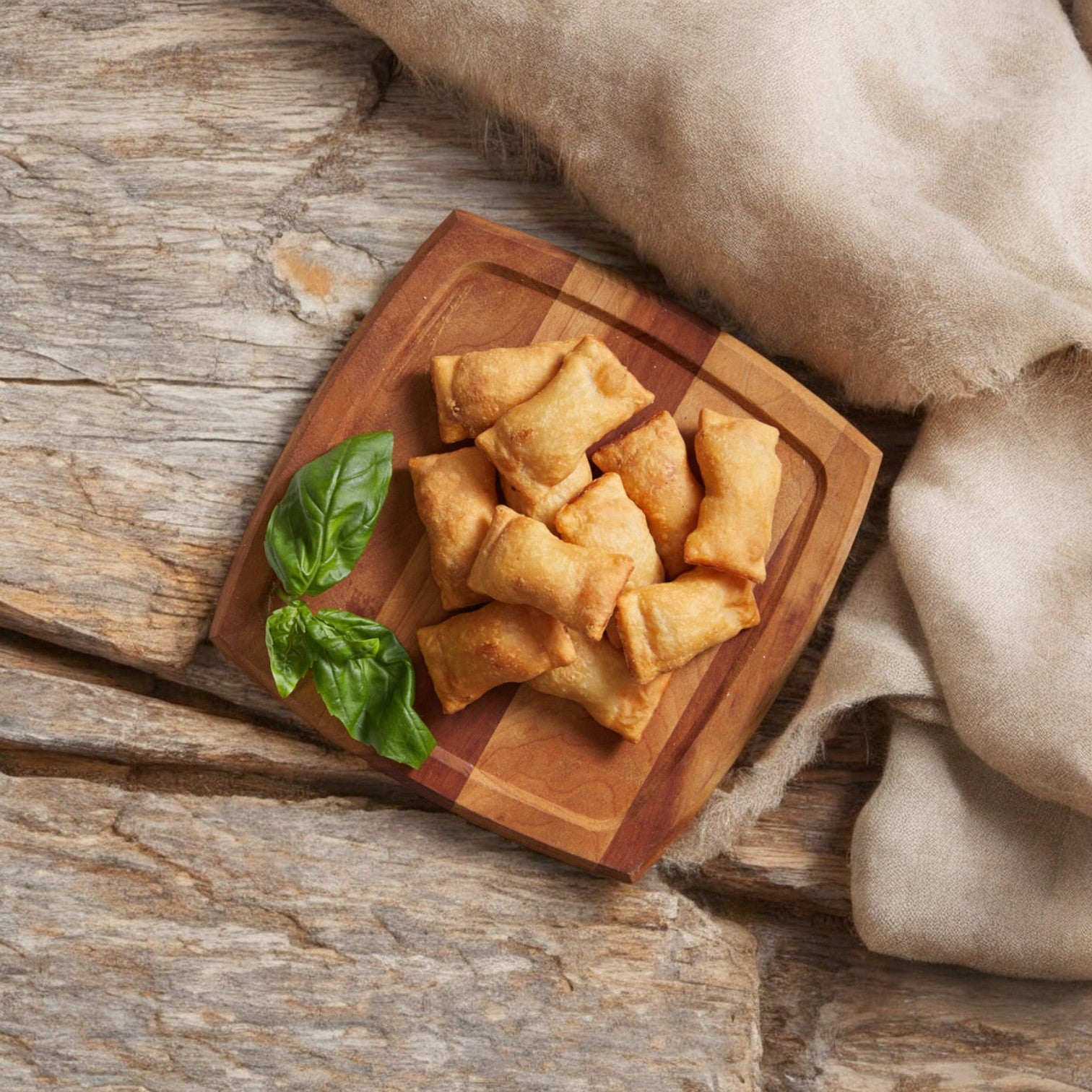 On a wooden plate, a small stack of Feel Good Foods Uncured Pepperoni Pizza Snacks with gluten-free crust is garnished with basil leaves. A beige fabric drapes over the wooden surface, enticing you to savor these delicious bites from Feel Good Foods.