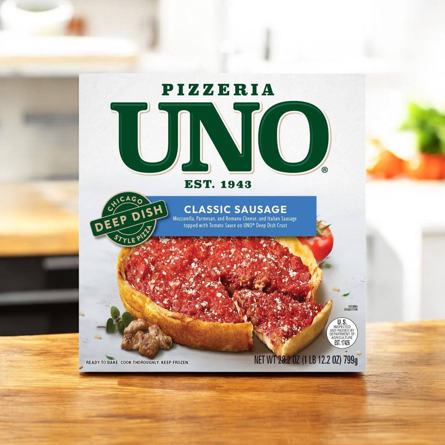 A 28.2 oz. box of Pizzeria Uno Classic Sausage Pizza sits on the countertop, displaying a tempting 9-inch Chicago-style deep dish with a slice enticingly removed.