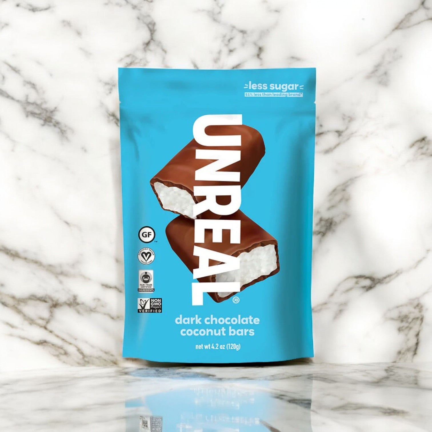 A package of Unreal Dark Chocolate Coconut Bars - 1 Count, encasing two chocolate-coated bars with a luscious white coconut filling, set against a white and grey marble background. These delightful treats are both Vegan and Gluten-Free, making them as mindful as they are enjoyable.