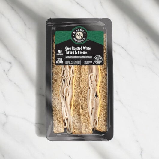 The E.A. Sween Oven Roasted Turkey & Cheese Sandwich Wedge features a 300-calorie, protein-rich (20g) combination of turkey and cheese on wheat bread, packaged in a black plastic container on a marble surface. The frozen product boasts up to 30 days of shelf life once refrigerated.