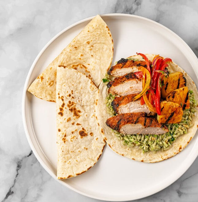 A platter featuring FoodHaul's Al Pastor Chicken Tacos, crafted from premium ingredients: a tortilla filled with grilled chicken, sliced peppers, pineapple, and green rice. An additional tortilla is enticingly folded beside it.