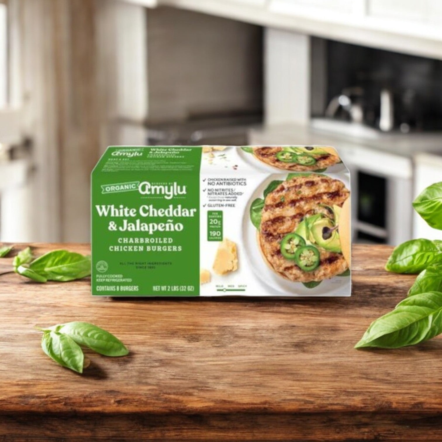 A box of Amylu’s 4-Pack Combo – Premium Chicken & Sausage Variety sits on a wooden kitchen table, with fresh basil leaves nearby, emphasizing the gluten-free, antibiotic-free delight inside.