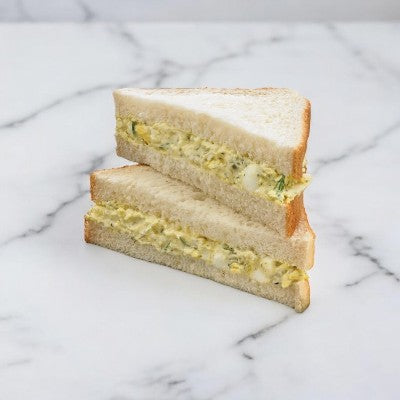 E.A. Sween's Dill Egg Salad on Homestyle White Bread Sandwich Wedge features two halves of an egg salad sandwich with a hint of dill pickle relish, artfully stacked on a marble surface. Ships frozen with a 30-day shelf life once removed from the freezer.
