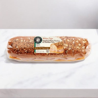 An E.A. Sween labeled Smoked Turkey & Cheddar Sub Sandwich on a rustic oat topped roll is placed on a white surface, showcasing visible oats and seeds.
