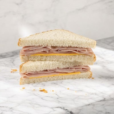 A halved Smoked Ham & Cheese Sandwich Wedge by E.A. Sween, featuring turkey on white bread, stacked on a marble surface, ready-to-eat after freezing with a 30-day cooler shelf life.