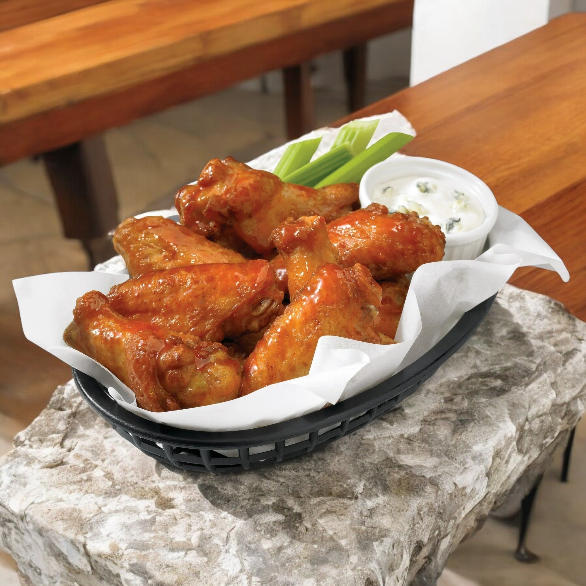A bag of Tyson Any’tizers Frozen Bone-In Buffalo Style Hot Wings, weighing 1.37 lbs, served with celery sticks and dipping sauce on a stone surface near wooden tables.