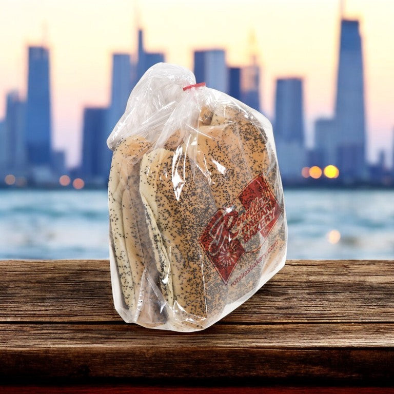 A case of Rotella's Poppyseed Sliced Hot Dog Buns rests on a wooden surface, with a blurred city skyline in the background.