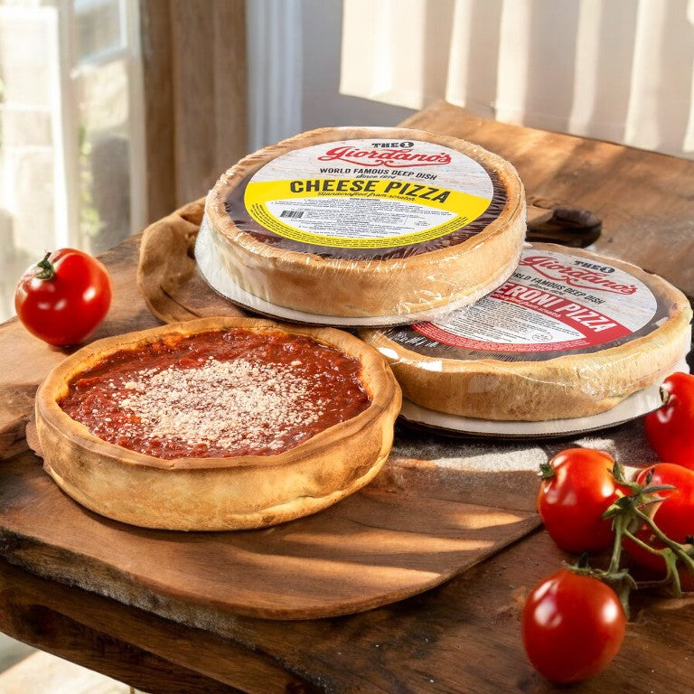 A wooden table hosts a Chicago deep-dish cheese pizza oozing with tomato sauce. In the background, two frozen pizzas labeled as cheese and pepperoni sit, surrounded by fresh tomatoes that evoke Giordano's authentic flavors. Meet the "Giordano's Deep Dish Pizza Combo Pack - 3 Deep Dish Pizzas!.