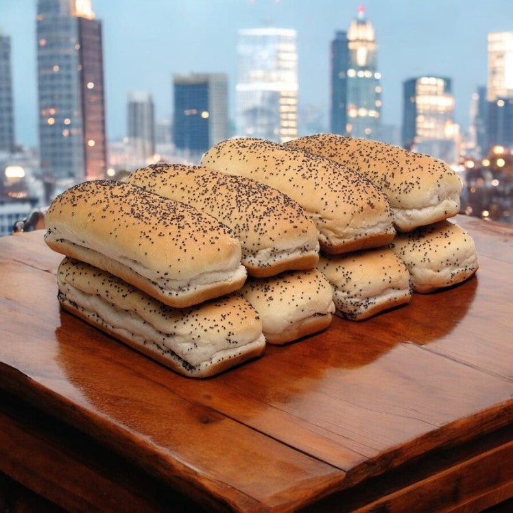 Vienna Beef Hot Dog Buns, White Poppy Seed 5" Sliced, are neatly stacked on a wooden table, while a city skyline forms the ideal urban backdrop.