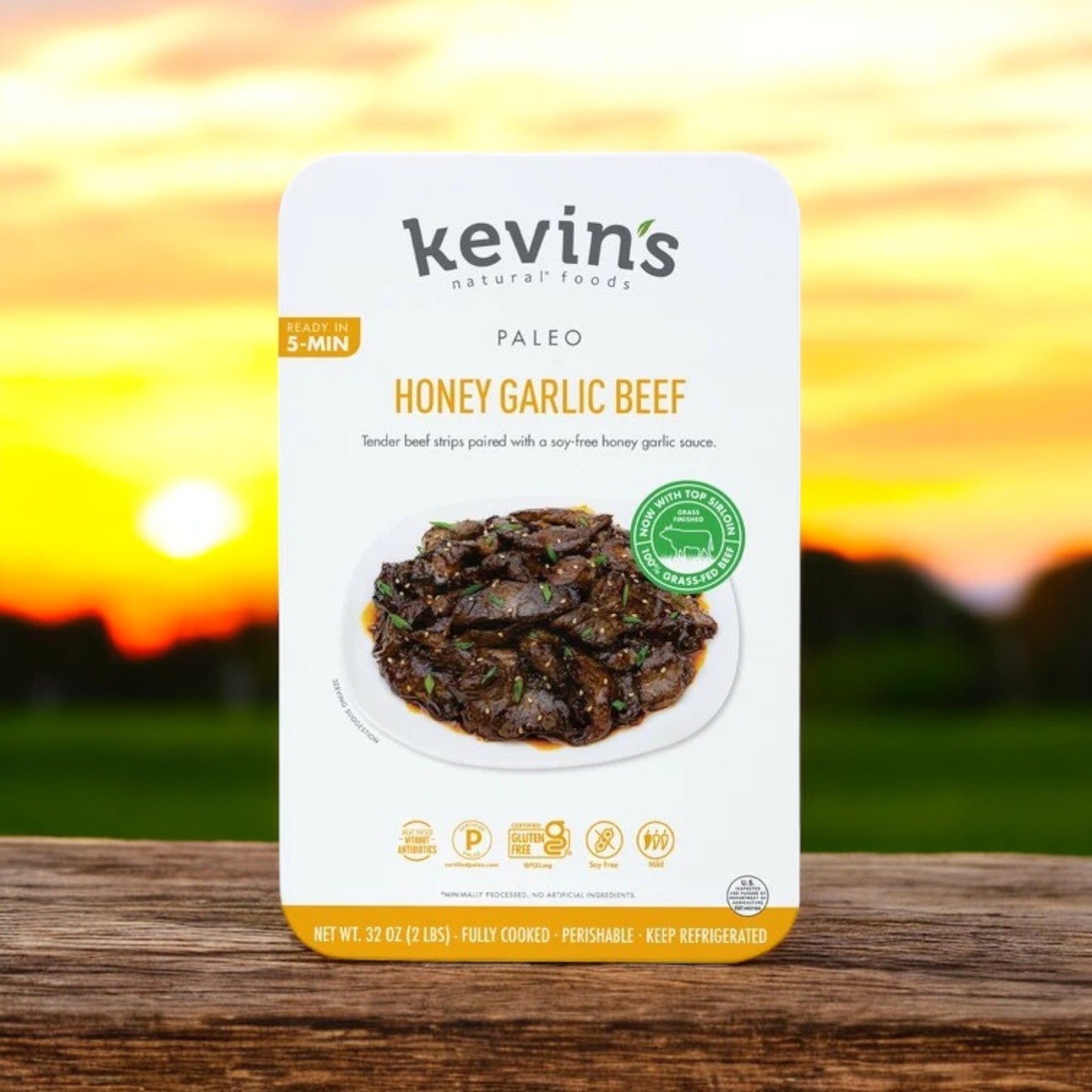 Kevin's Honey Garlic Beef, 32 oz. case featuring 4 packs, showcases its all-natural ingredients with succulent beef strips in sauce and a sunset background. This gluten-free delight ships frozen and lasts 30 days after defrosting.