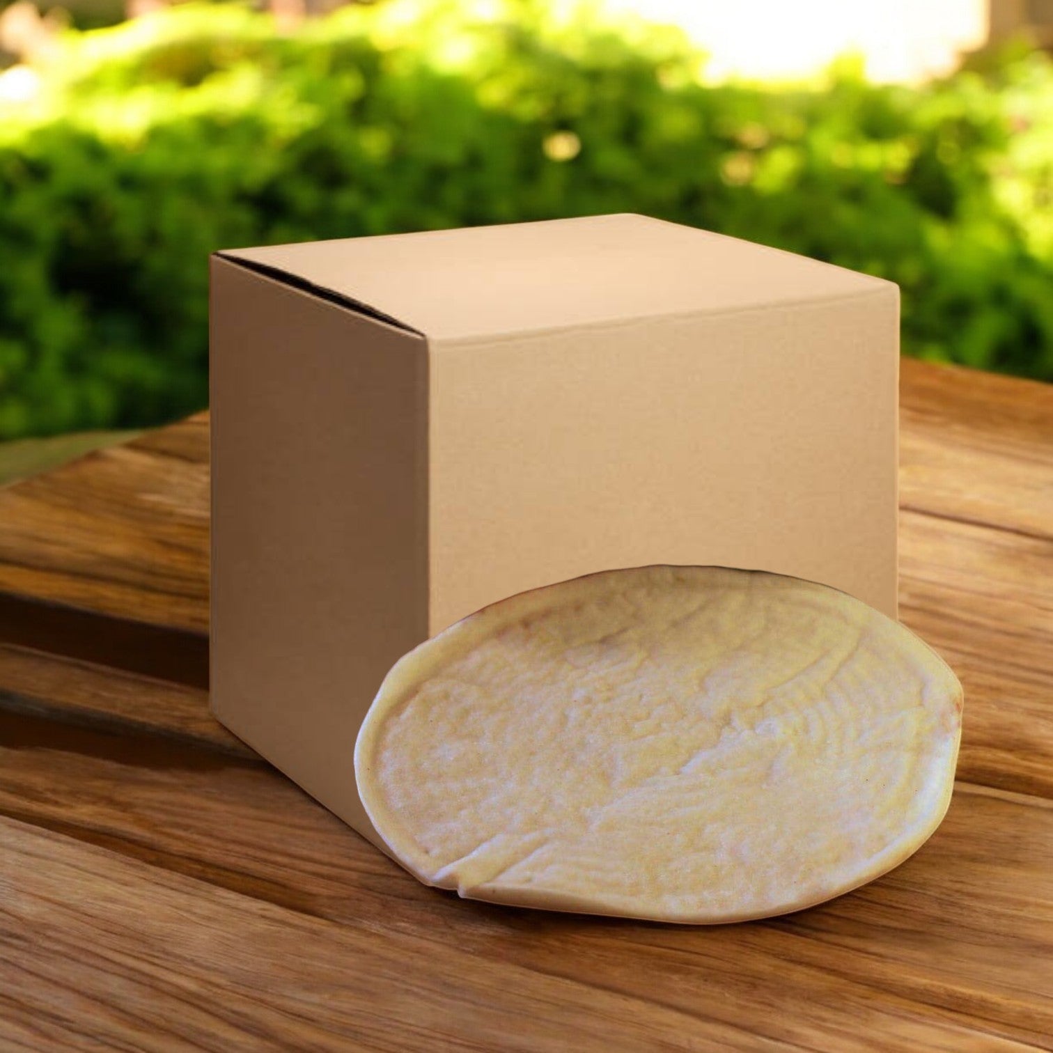 A Venice Bakery Gluten Free Vegan Plain Pizza Crust, 10 Inch, is partially inserted into a cardboard box on a wooden surface outdoors.