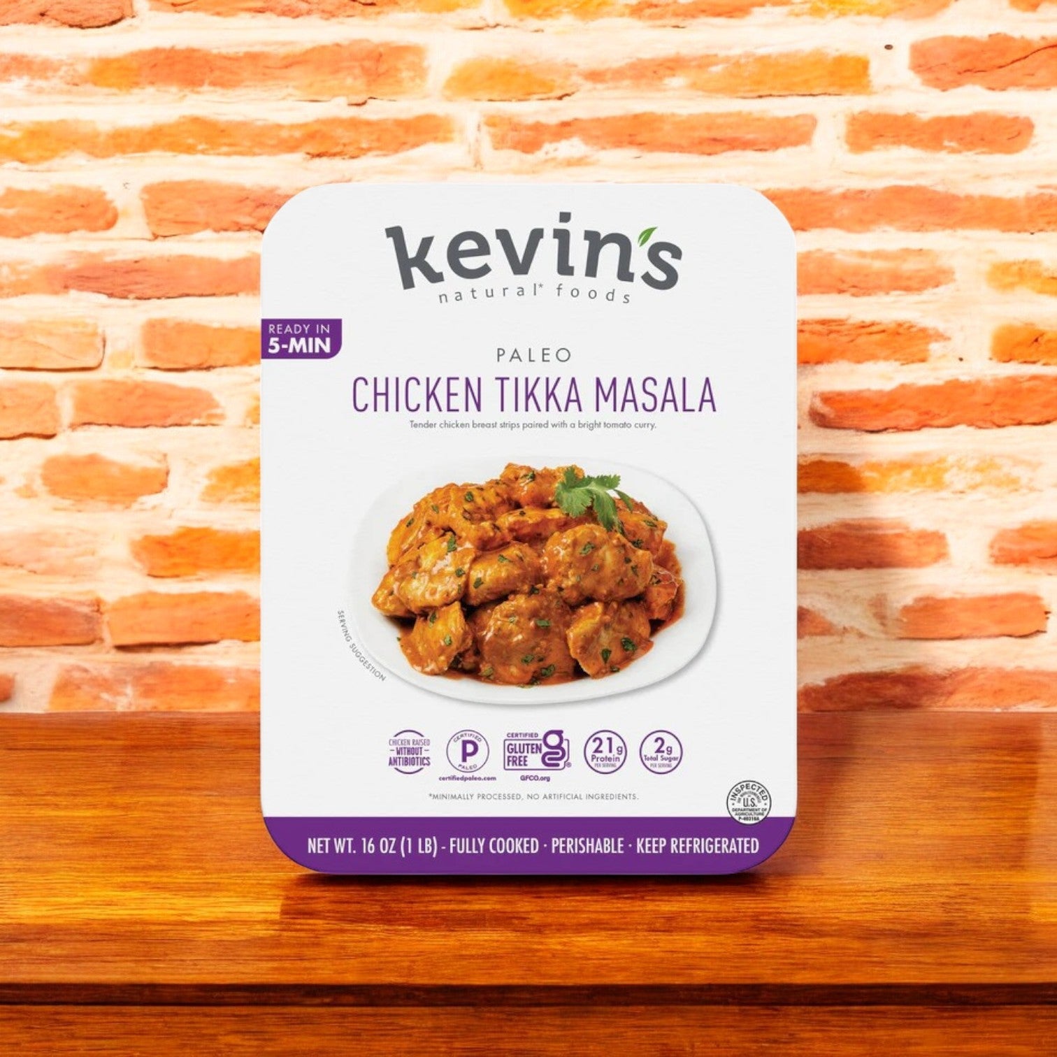Kevin's Chicken Tikka Masala - 16 oz. package, set against a brick wall background, offers authentic Indian cuisine ready in just 5 minutes. Crafted with all-natural ingredients, it's gluten-free and contains 21 grams of protein per serving.