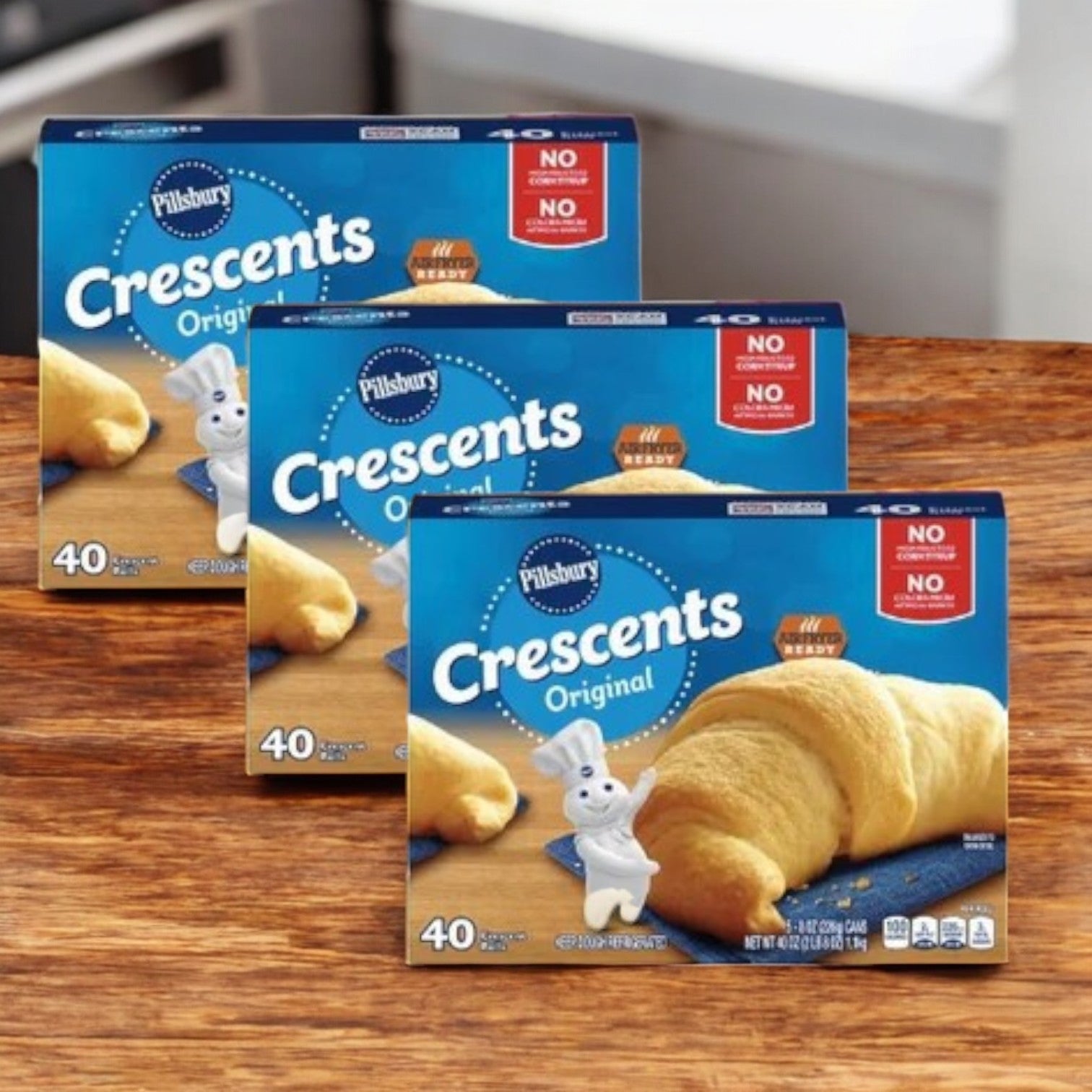 Three packs of Pillsbury Crescents- 3 Count are on a wooden surface, offering 40 flaky, buttery crescent rolls each. The blue packaging showcases the Doughboy mascot and guarantees no high fructose corn syrup.