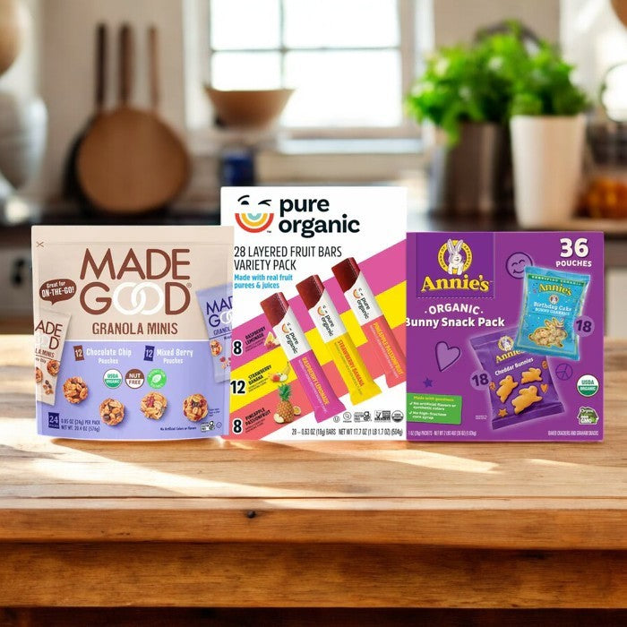 Three wholesome snack boxes on a wooden table: Made Good Granola Minis, Pure Organic Layered Fruit Bars, and Annie's Organic Bunny Snack Pack. All individually wrapped and featured in Easy Lunches' "Kids Snack Pack! 3 Items!" with a blurred kitchen background.