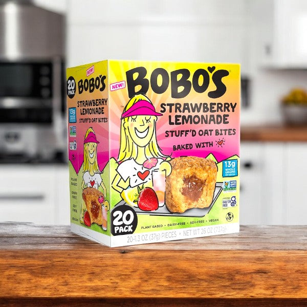 On the kitchen counter sits a box of Bobo's Stuff'd Oat Bites, Strawberry Lemonade flavor, 1.3 oz, 20 count. The packaging displays a cheerful illustration of a smiling person holding an oat bite filled with refreshing strawberry lemonade.