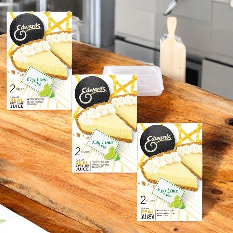 Three boxes of Edwards Desserts Key Lime Pie-3 Count slices rest alluringly on a wooden kitchen table, featuring their delicious graham cracker crust. Ideal for enthusiasts of indulgent frozen desserts.
