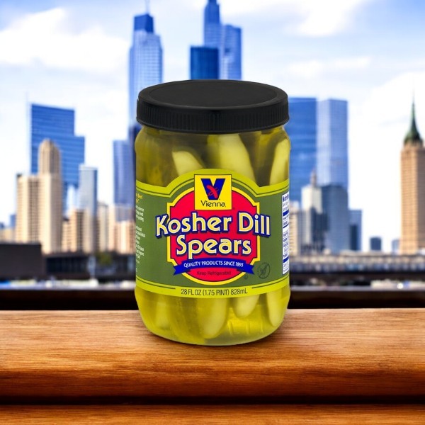 A Vienna Hot Dog Kit! Chicago Style! featuring 32 hot dogs with condiments and buns sits on a wooden surface, the blurred city skyline behind it inspiring thoughts of the perfect Chicago-style hot dog feast.