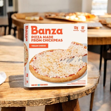 A box of Banza Vegan Cheese Pizza, featuring a gluten-free chickpea crust, sits on a wooden table.