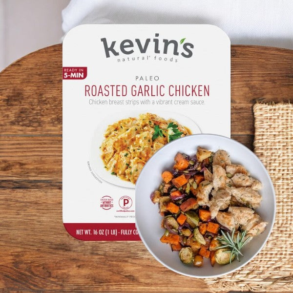 Kevin's Natural Foods Roasted Garlic Chicken package showcases an enticing image of a garlic chicken and vegetable dish on a rustic wooden surface, highlighting its keto-friendly, paleo-certified benefits.