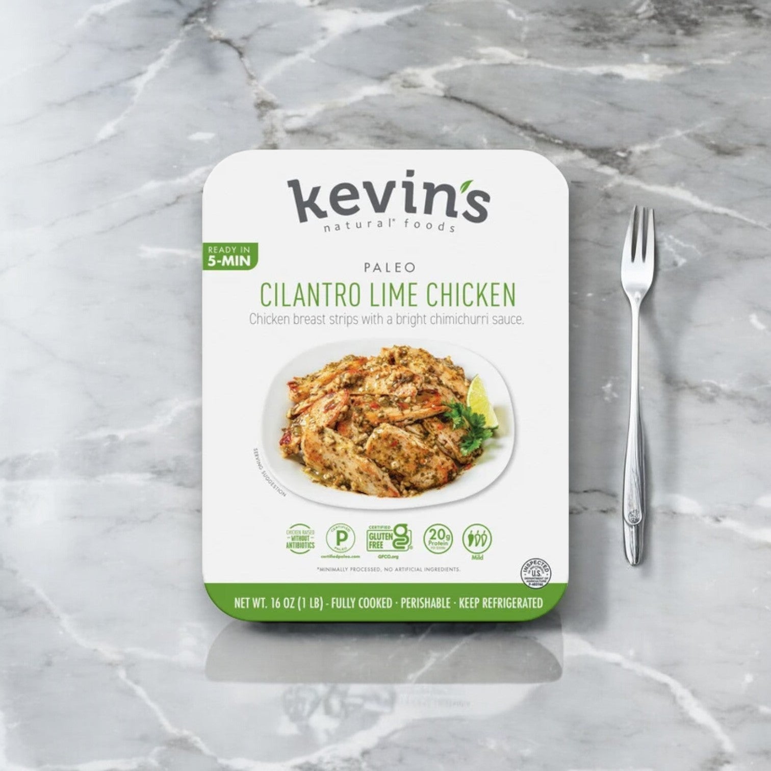 Kevin's Cilantro Lime Chicken - 16 oz. (1 Case, 4 Pack) is packaged with care on a marble surface, featuring a fork beside it. The vibrant cilantro lime sauce promises an elevated dining experience. Ships frozen; lasts 30 days in the cooler once out of the freezer!.