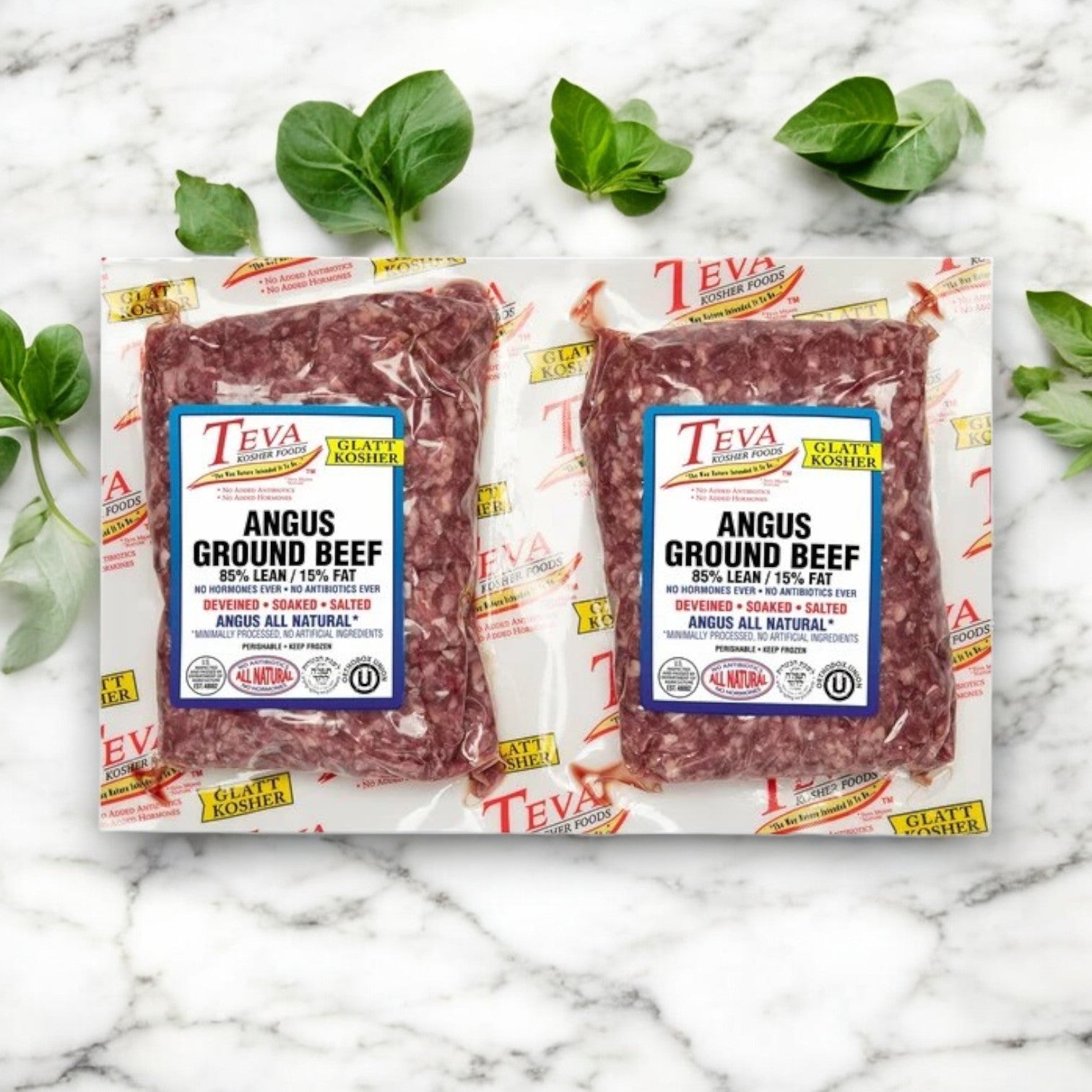 Two 3 lb. packs of Teva Kosher Foods Glatt Kosher Angus Ground Beef, 85% lean, rest on a marble surface with green leaves. The packaging highlights "Kosher" and "Glatt Kosher," indicating its premium quality.