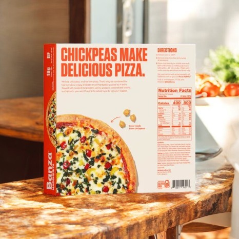 A Banza Roasted Veggie Pizza-3 Count box with a cauliflower crust and chickpeas as key ingredients sits on a wooden table. The back displays nutritional info and cooking instructions for this tasty gluten-free pizza.