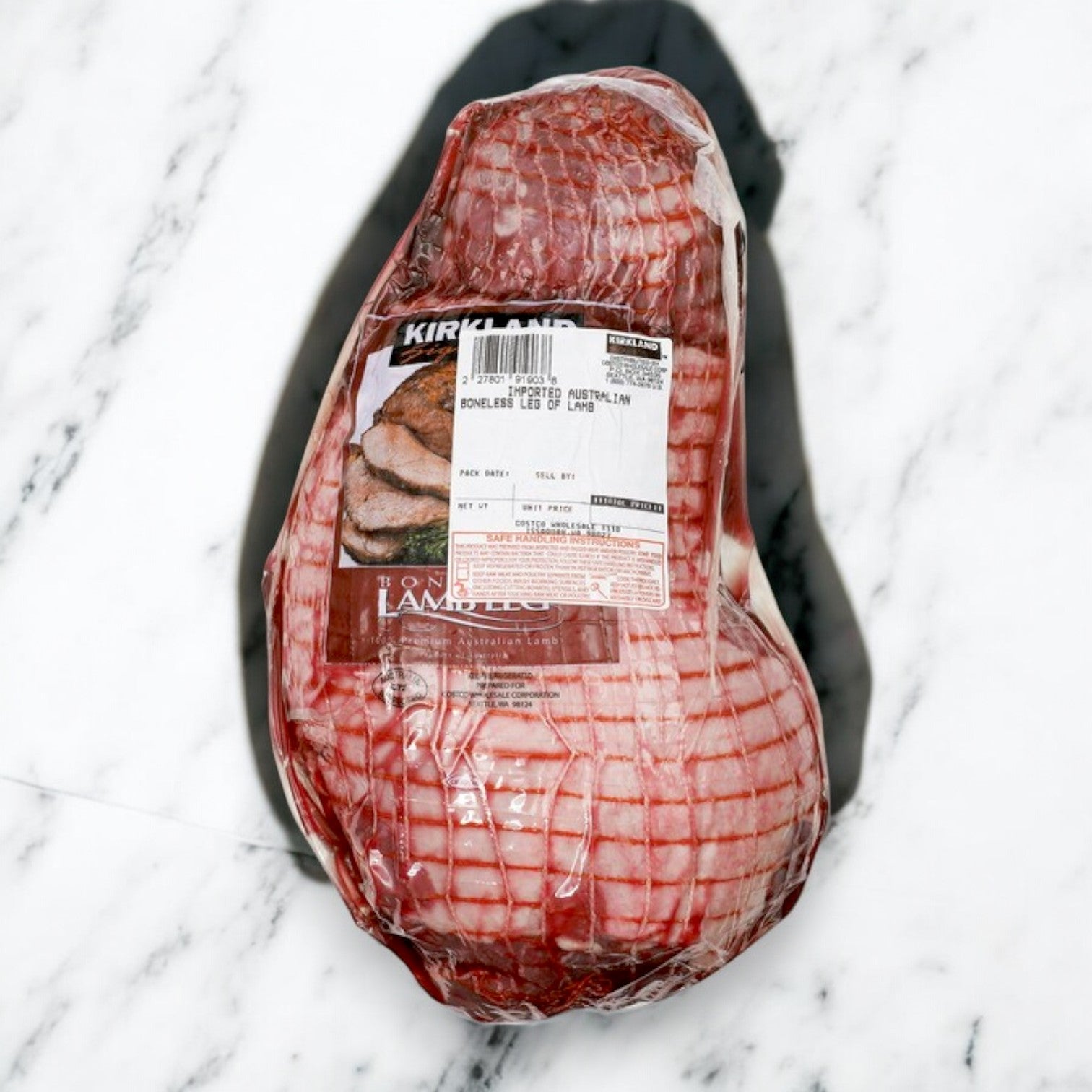The Kirkland Signature Halal Boneless Leg of Lamb, 5 lb Avg wt, is ethically sourced and wrapped in clear plastic with a label, ensuring premium tenderness and excellence in every bite on a marble surface.