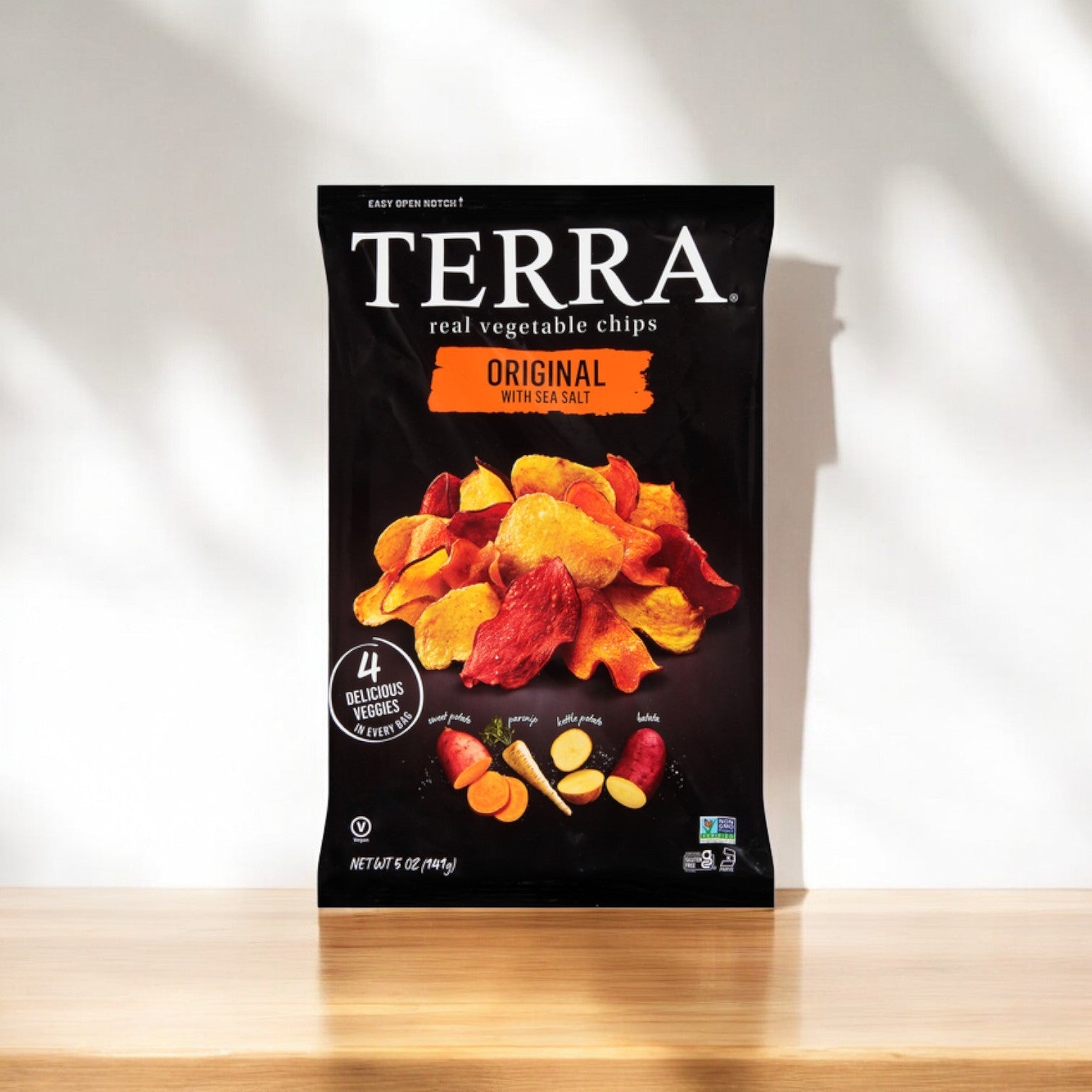 A Terra Original Chips bag, offering real vegetable chips with sea salt, sits on wood. The packaging showcases "4 delicious root vegetables" and is marked as non-GMO and gluten-free, ideal for a healthy snack.