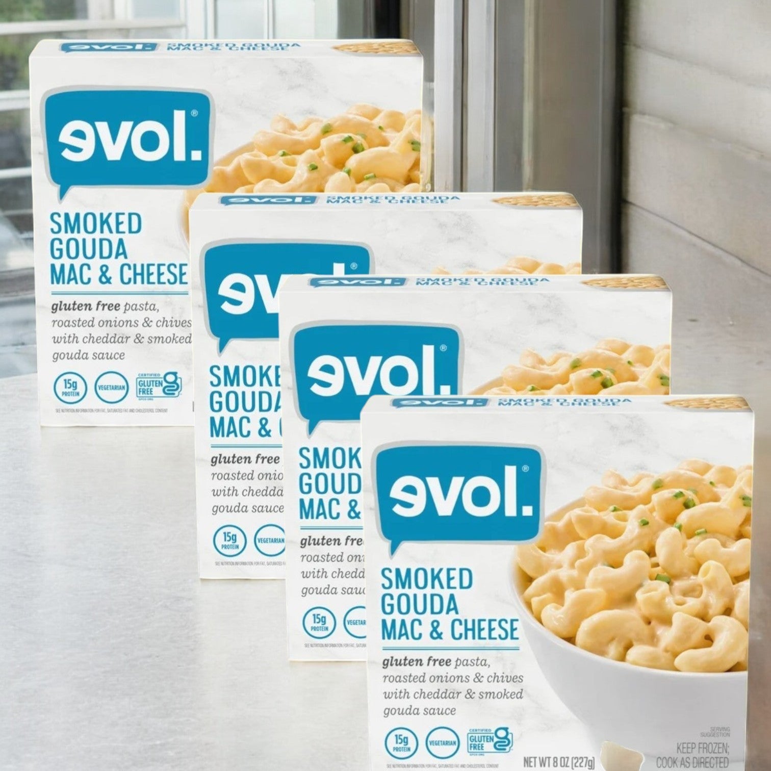 Evol's Gluten Free Smoked Gouda Mac and Cheese frozen meals, in 8 oz. boxes and a 4-count package, are neatly arranged on the kitchen counter.