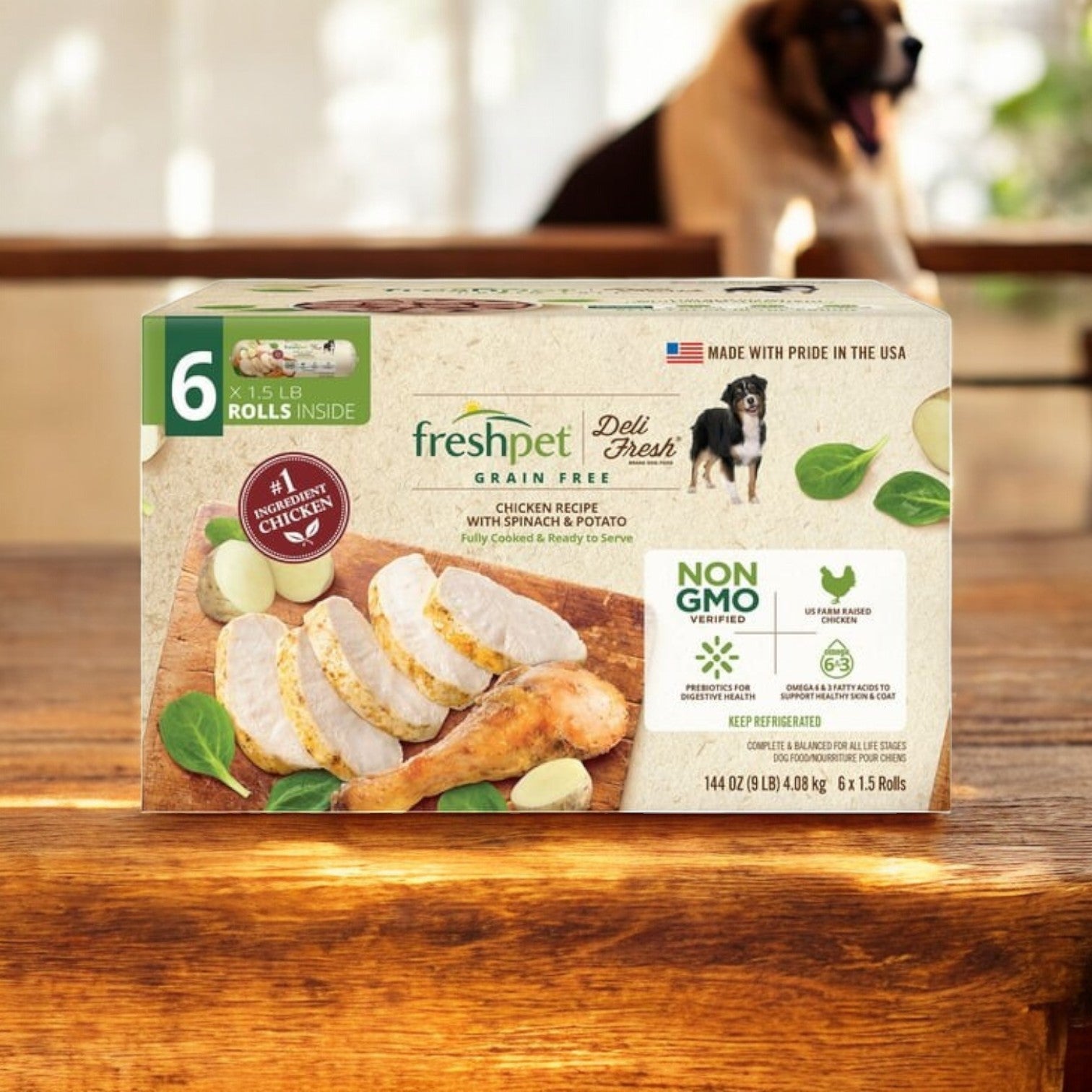 On a wooden table sits a box of Freshpet Deli Fresh Grain-Free Chicken Recipe Rolls, showcasing nutrient-rich sliced chicken, spinach, and potato images. In the background is a blurred dog excited for the high-quality protein meal. Enjoy free shipping with 3 boxes from Freshpet!.