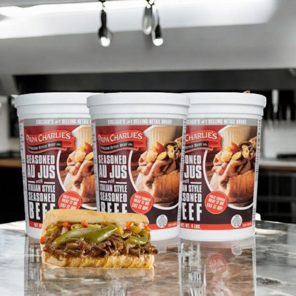 Three tubs of Papa Charlie's Italian Beef (4 lbs each, 3 count) sit on a kitchen counter behind a Chicago-style beef sandwich garnished with peppers, delivering authentic Italian flavors in every bite.