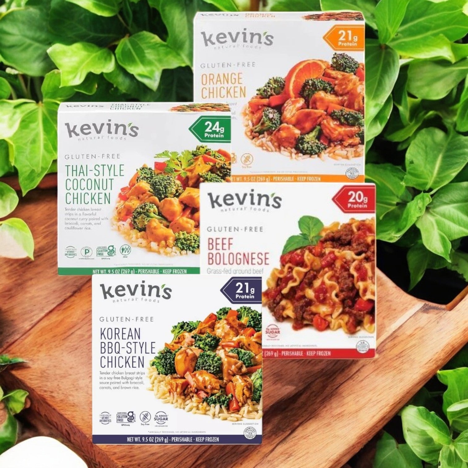 Four boxes of Kevin's 4 Pack Combo - Gluten-Free Gourmet Meals, 9.5 oz each, are displayed against a leafy backdrop, featuring Orange Chicken, Thai-Style Coconut Chicken, Beef Bolognese, and Korean BBQ-Style Chicken.
