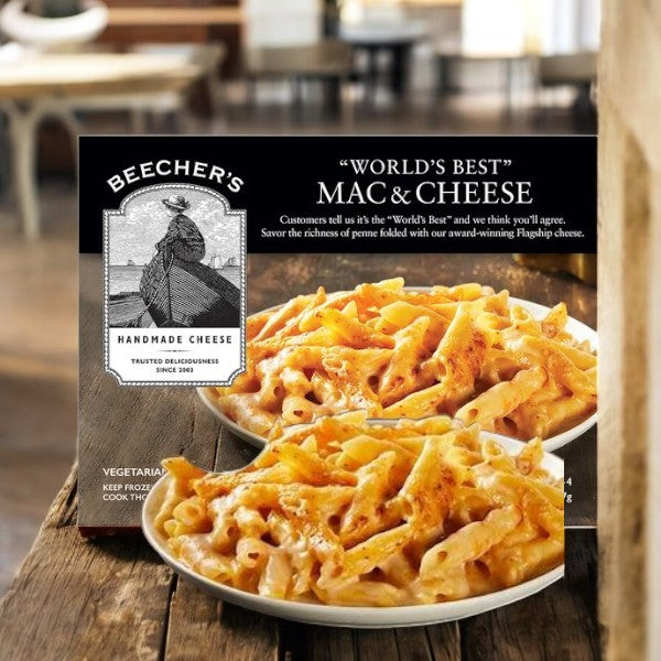 A box of Beecher's "World's Best" Mac & Cheese-1 Count is on a wooden surface, with a bowl of the rich aged cheddar delight from Beecher's ready to enjoy in front.