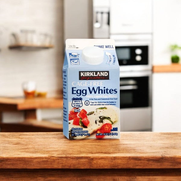 A case of Kirkland Signature Liquid Egg Whites, Cage Free-6 Count rests on a wooden countertop in a cozy kitchen setting.