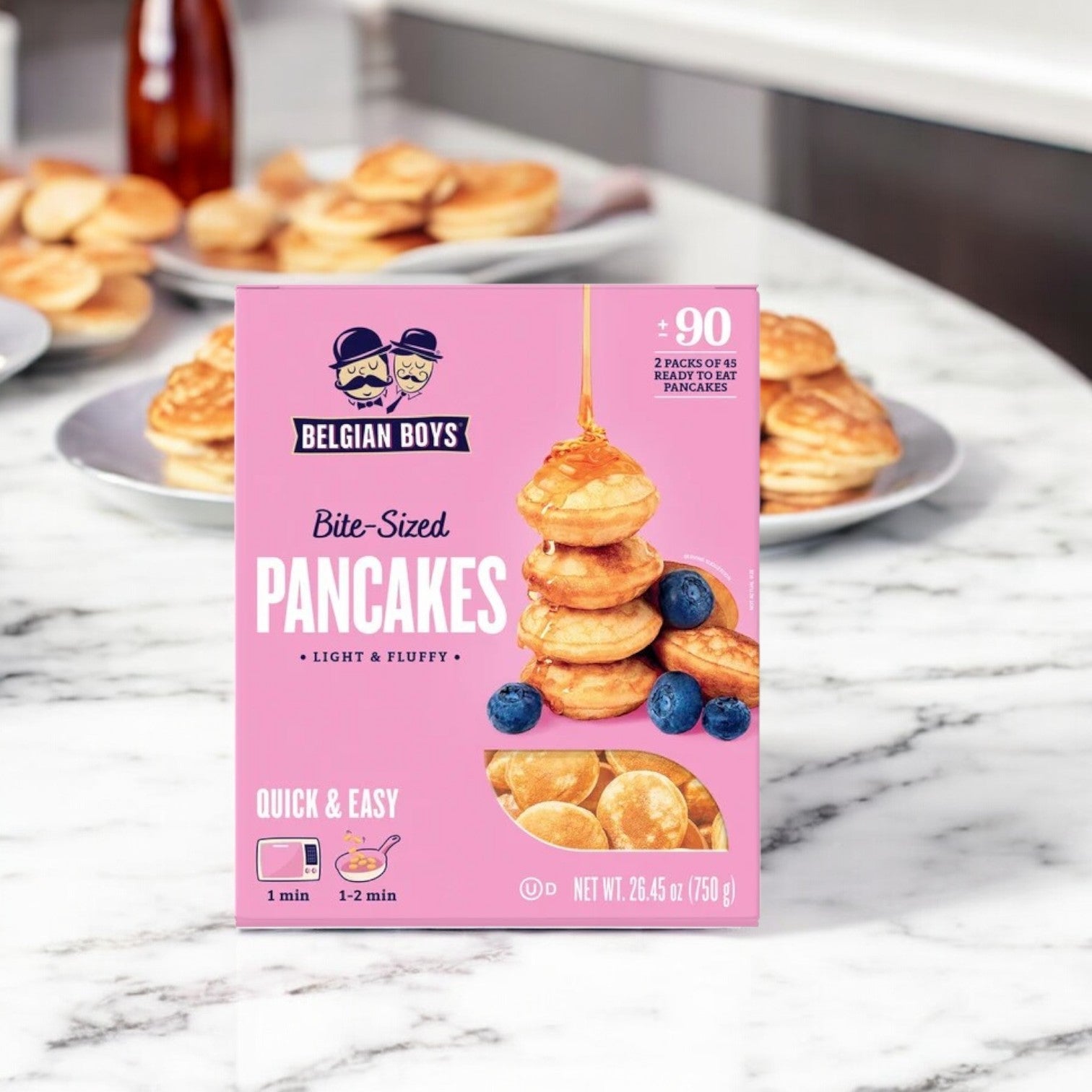 A box of Belgian Boys Refrigerated Bite-Sized Pancakes-1 Count sits on a marble countertop, encircled by small stacks of these delightful treats.