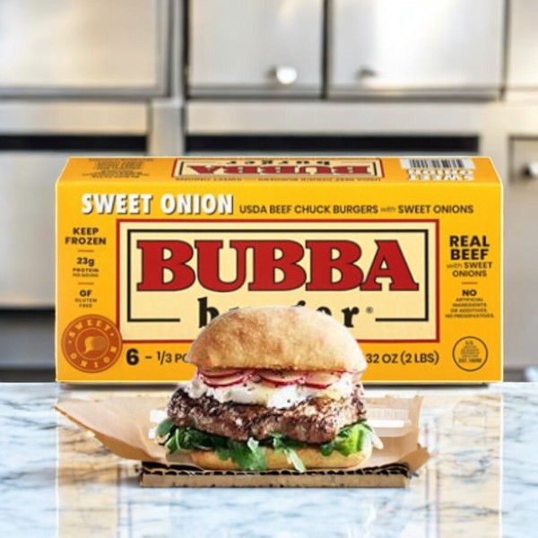 A Bubba Burger Beef Chuck, Sweet Onion 6-pack sits behind a deliciously cooked burger with beef chuck, crisp greens, onion slices, and savory sauce on a bun, elegantly presented on a cardboard tray.