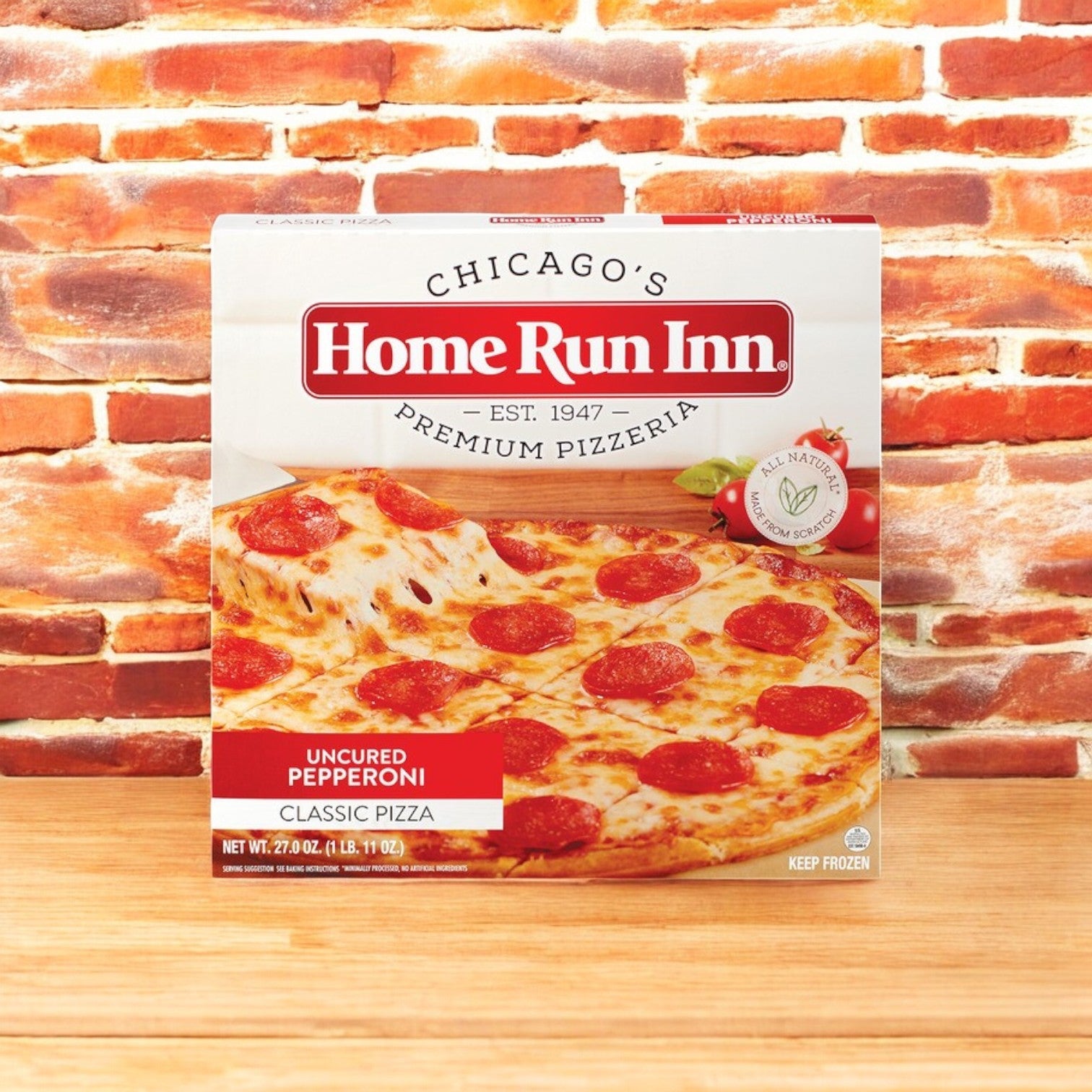 A box from the Easy Lunches Eli's Cheesecake Celebration Sampler & Home Run Inn Pizza Combo rests against a brick wall, capturing the authentic Chicago-style pizza vibe.