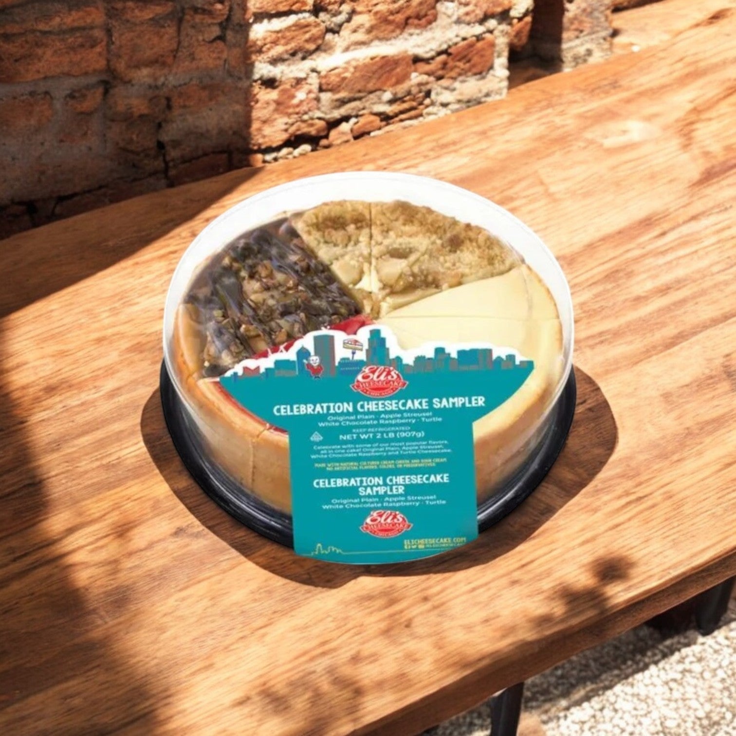 An Eli's Cheesecake Celebration Sampler & Home Run Inn Pizza Combo by Easy Lunches sits on a wooden table outdoors, near a brick wall—ideal for dessert lovers like Chicago-style pizza fans appreciate their deep dish.