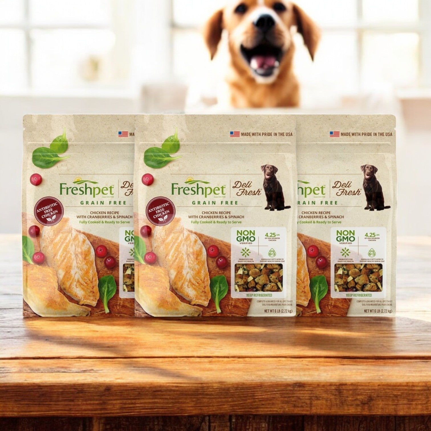 Three boxes of Freshpet Deli Fresh Dog Food, Chicken with Cranberries & Spinach, are on a wooden table with a blurred dog in the background.