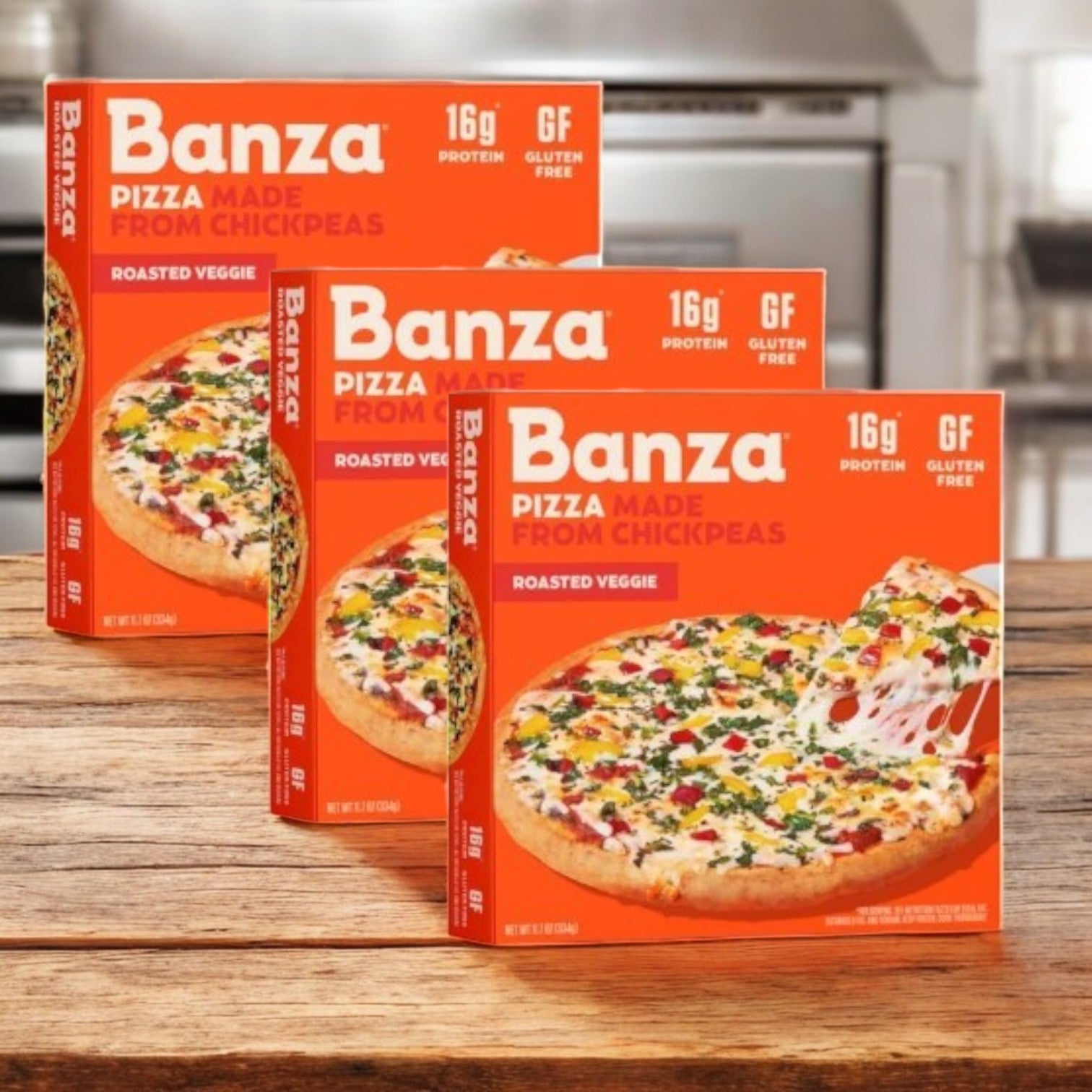 Three boxes of Banza Roasted Veggie Pizza are showcased in a kitchen, emphasizing 16g protein per serving and featuring a gluten-free cauliflower crust.