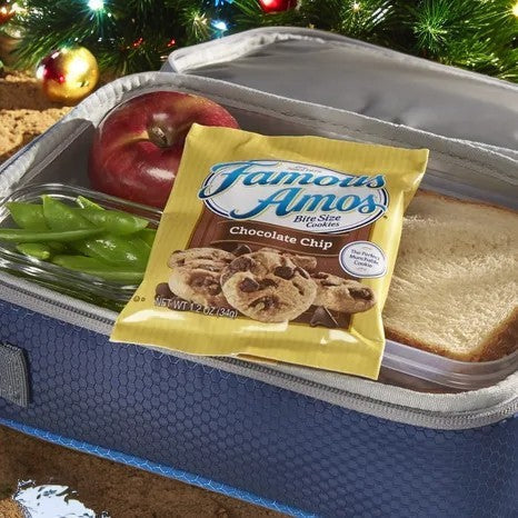 A lunchbox includes a sandwich, an apple, and a glass container of green beans, perfectly complemented by Famous Amos Chocolate Chip Cookies from the 42 Pack-1 Count. Festive holiday decorations set the scene in the background.