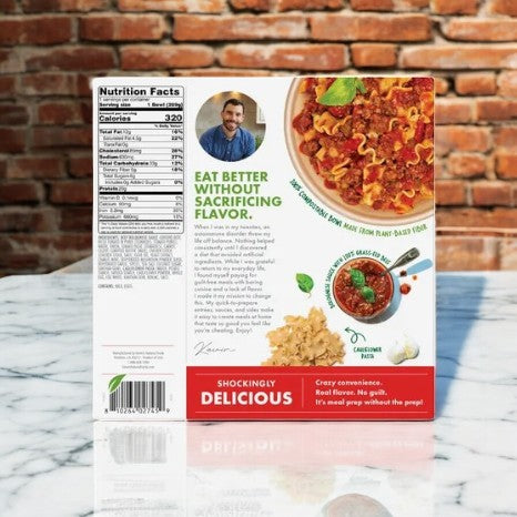 Kevin's Natural Foods Beef Bolognese-1 Count package displays a delicious meal with serving suggestion image and nutritional facts. It highlights plant-based benefits and keto-friendly options, includes a chef's note, all set against a brick wall background.