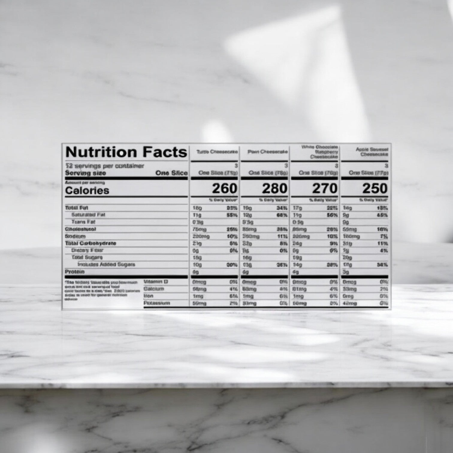 A nutrition facts label sits on a marble surface, outlining the calorie and nutritional information for each slice in the Eli's Cheesecake Celebration Sampler. Ideal for those looking to enjoy a range of cheesecake flavors while making informed decisions during their sampler celebrations.