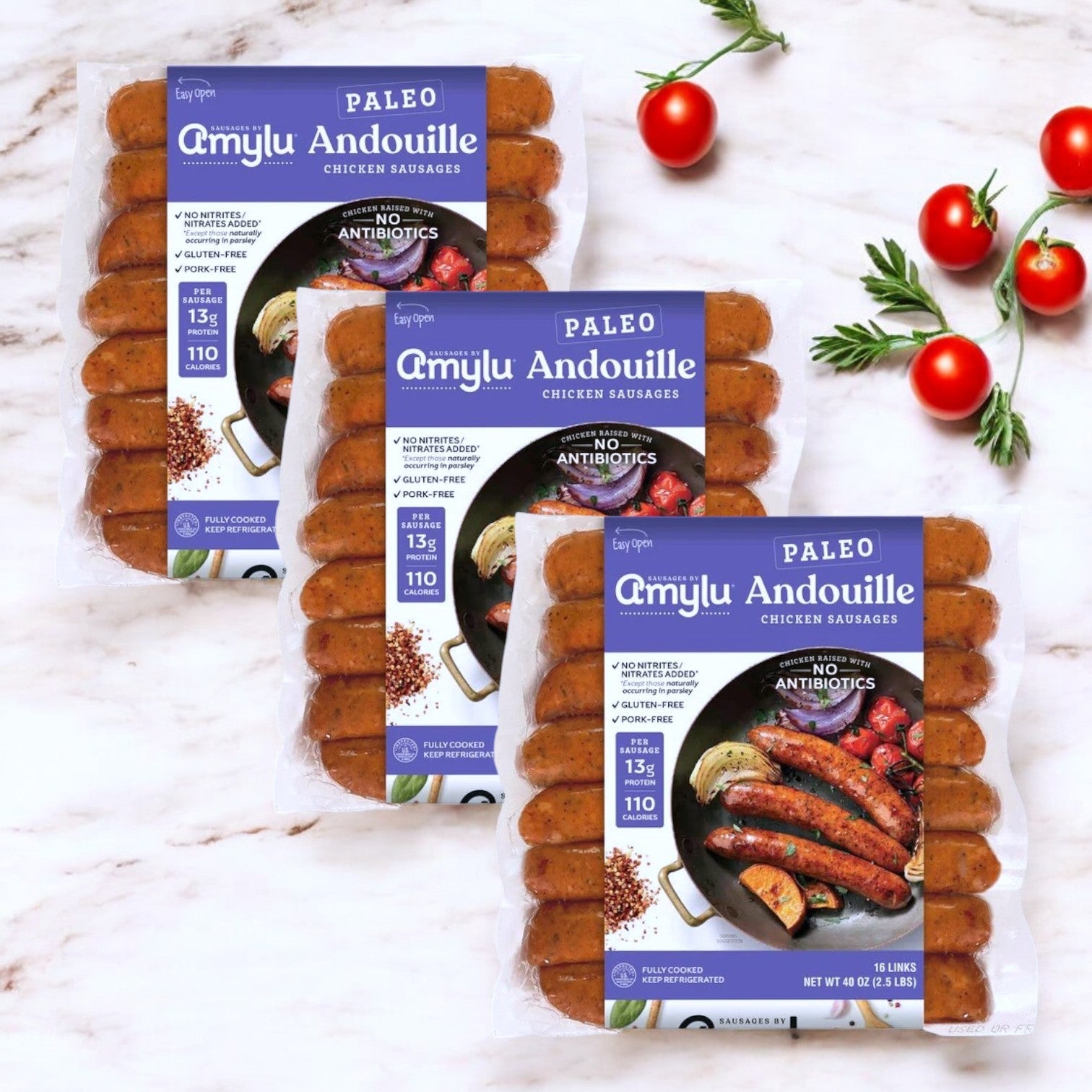 Three packs of Amylu Paleo Andouille Sausage (16-count) are shown on a marble surface with cherry tomatoes. The packaging emphasizes its high protein content and no antibiotics, making it a great paleo-friendly choice.