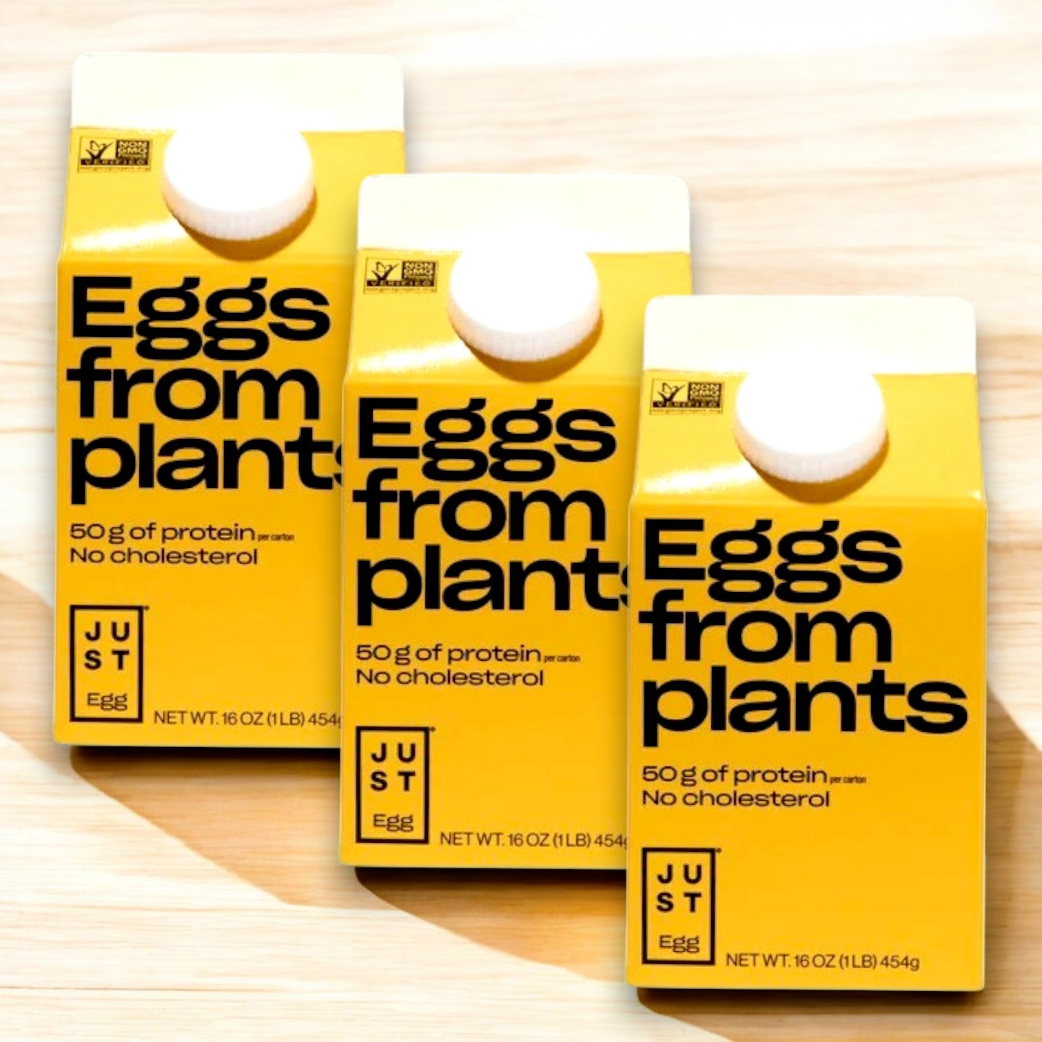 Three yellow Just Egg Plant-Based Egg cartons (48 oz) with "Eggs from plants," showcasing "50g of protein" and "No cholesterol," sit on a light wooden surface.