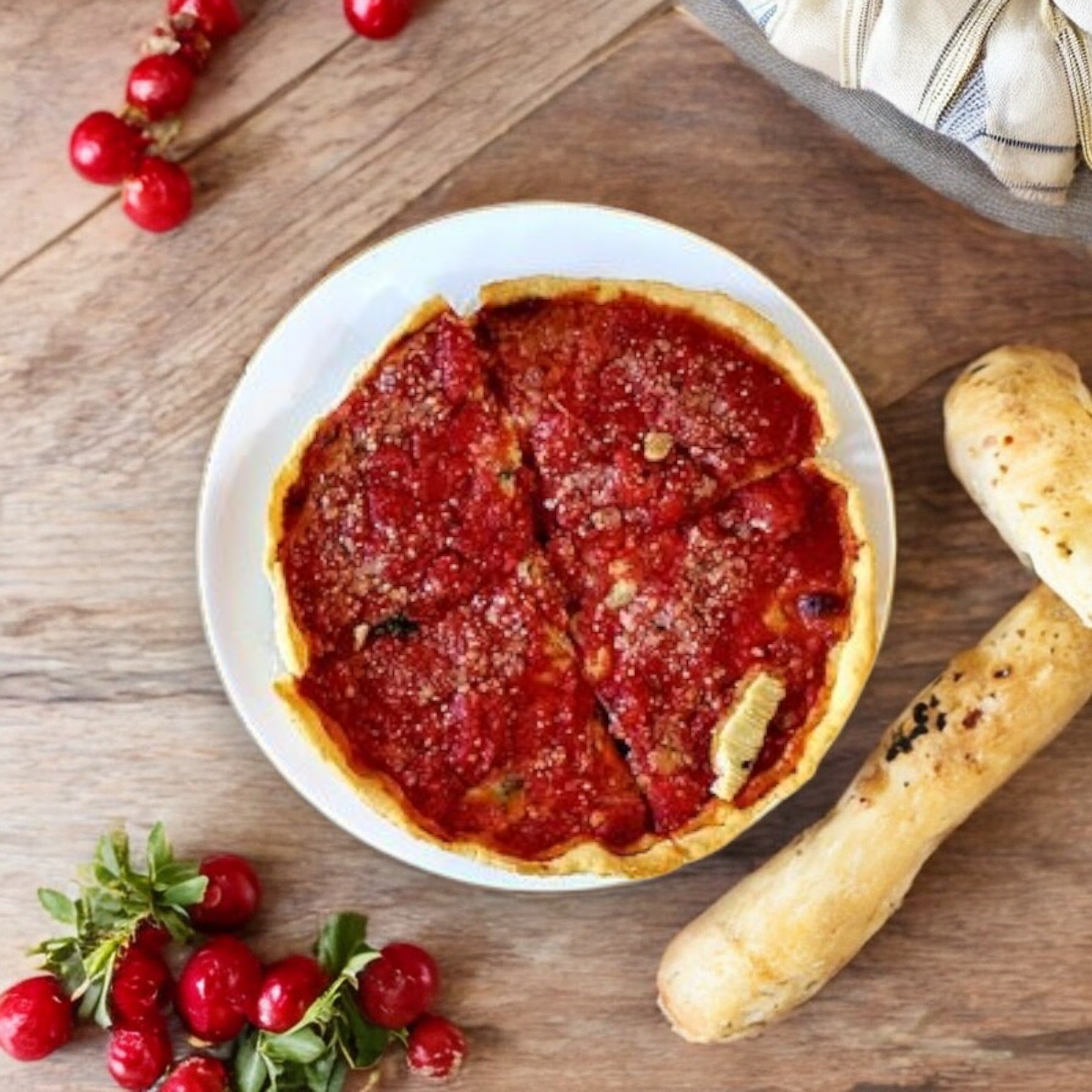A Lou Malnati's Spinach pizza, weighing 23 oz., is placed on a wooden table next to fresh cranberries and two breadsticks.