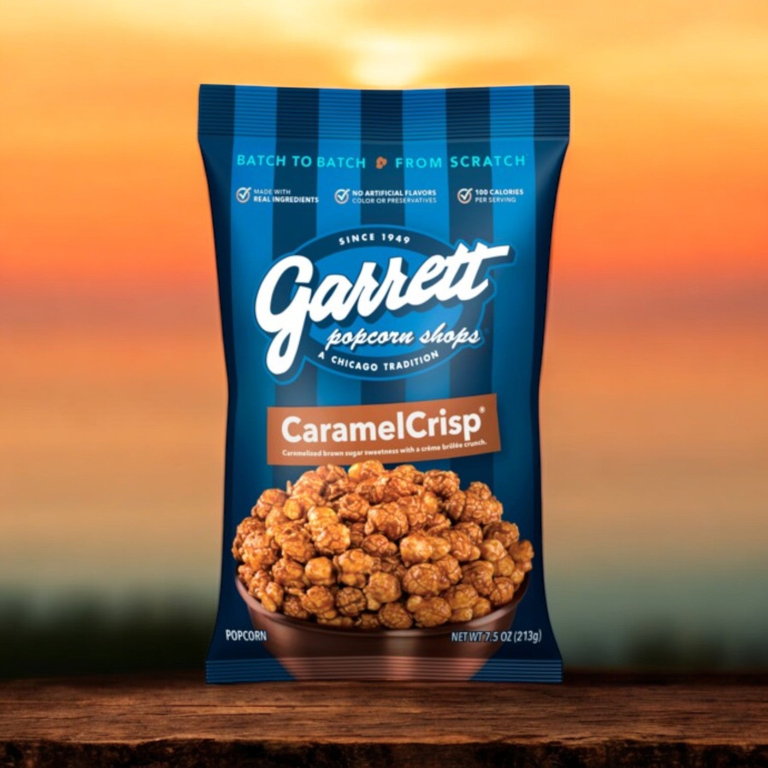 A 7.5 oz bag of Garrett Popcorn CaramelCrisp® is set against a sunset, highlighting its gourmet appeal. The packaging emphasizes real ingredients and no preservatives, inviting you to indulge in this savory snack.