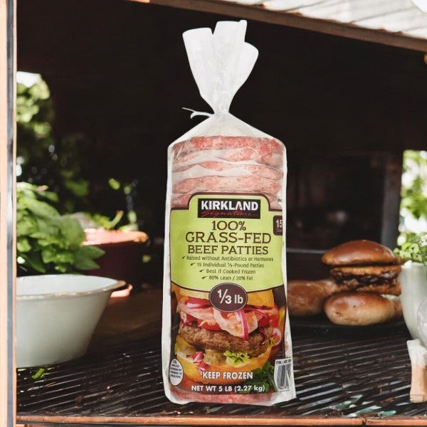 A 5 lb package of Kirkland Signature Grass-Fed Beef Patties—antibiotic-free, each patty weighing 1/3 lb—sits on the table with a cooked burger in the background.