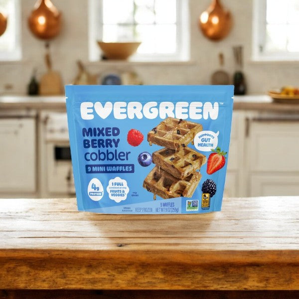 A package of Evergreen 3-Pack Combo – Mini Waffles Variety Pack rests on a wooden kitchen counter, with a kitchen visible in the background.